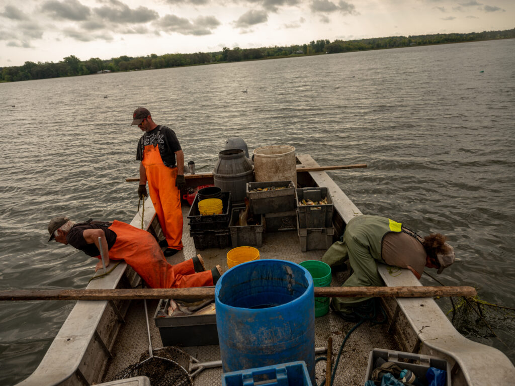 A photo of Kendall Dewey leaning over their fishing boat while Joanne Dewey pulls loose rope through a loop so that it holds until they visit the net again.