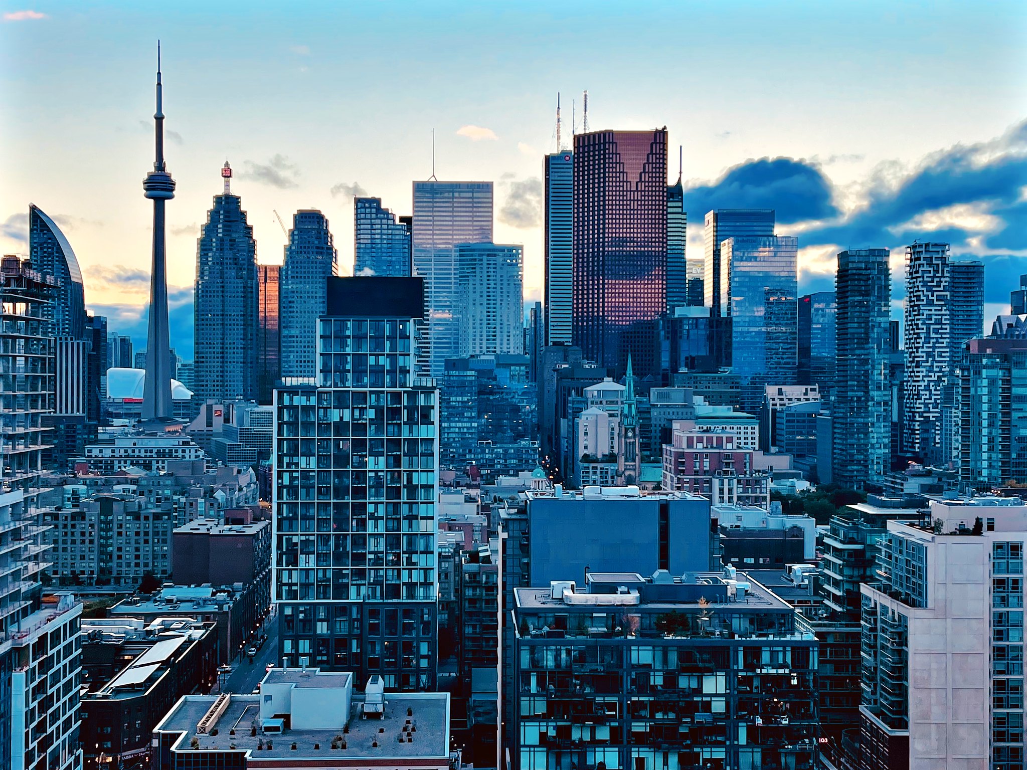 A blue-tinted shot of a city at dusk. A radio tower is in the background.