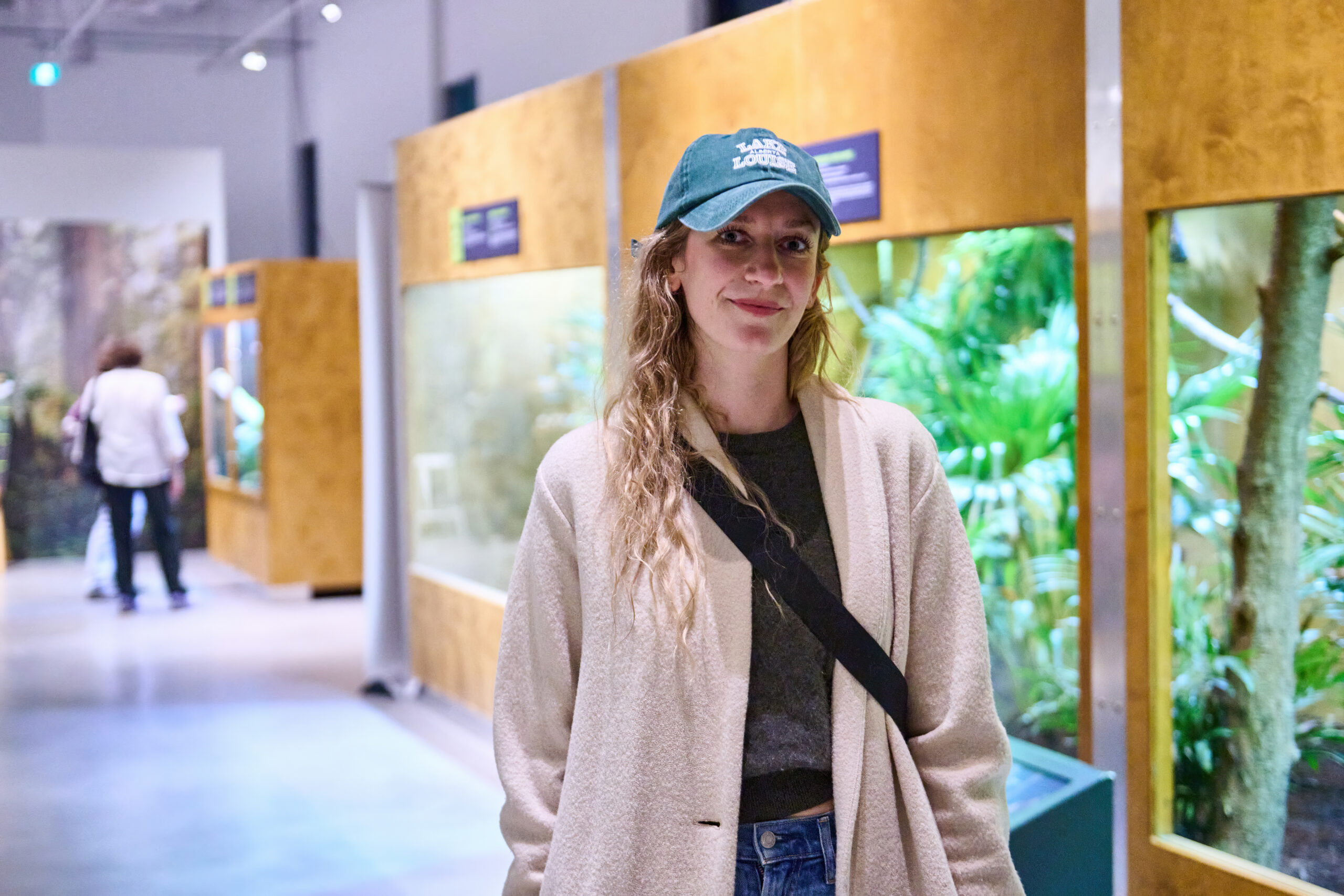 Woman with blue hat standing in a hallway of a museum with an exhibit of a sloth behind her.