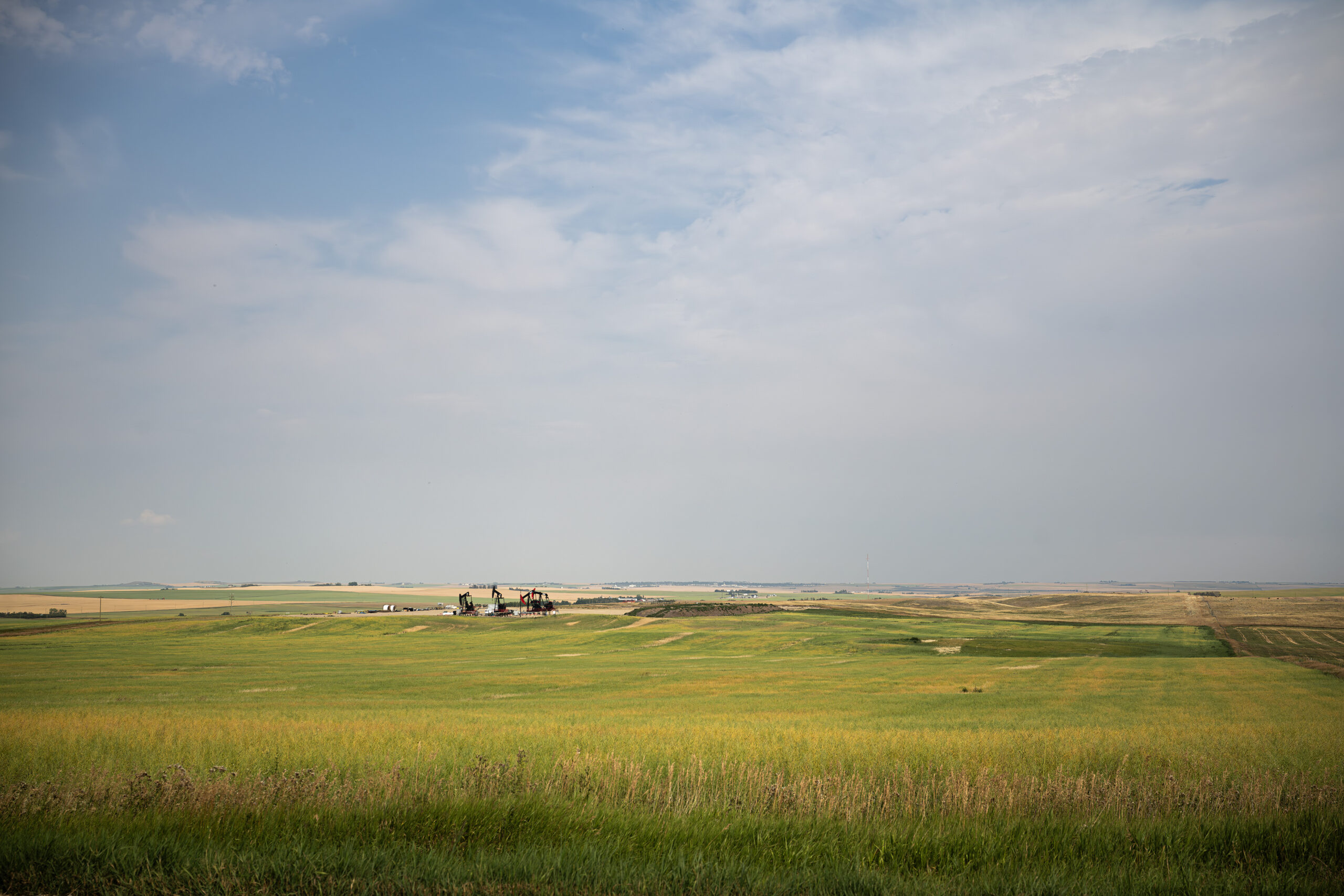 A view of prairie and big skies with oil and gas development on the horizon