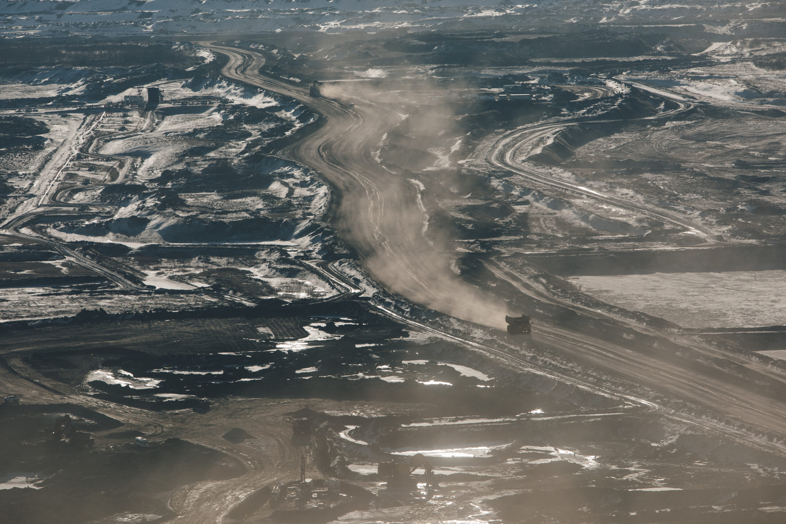 Aerial shot of muddy brown surface extending as far as the eye can see with a tiny dump truck far below