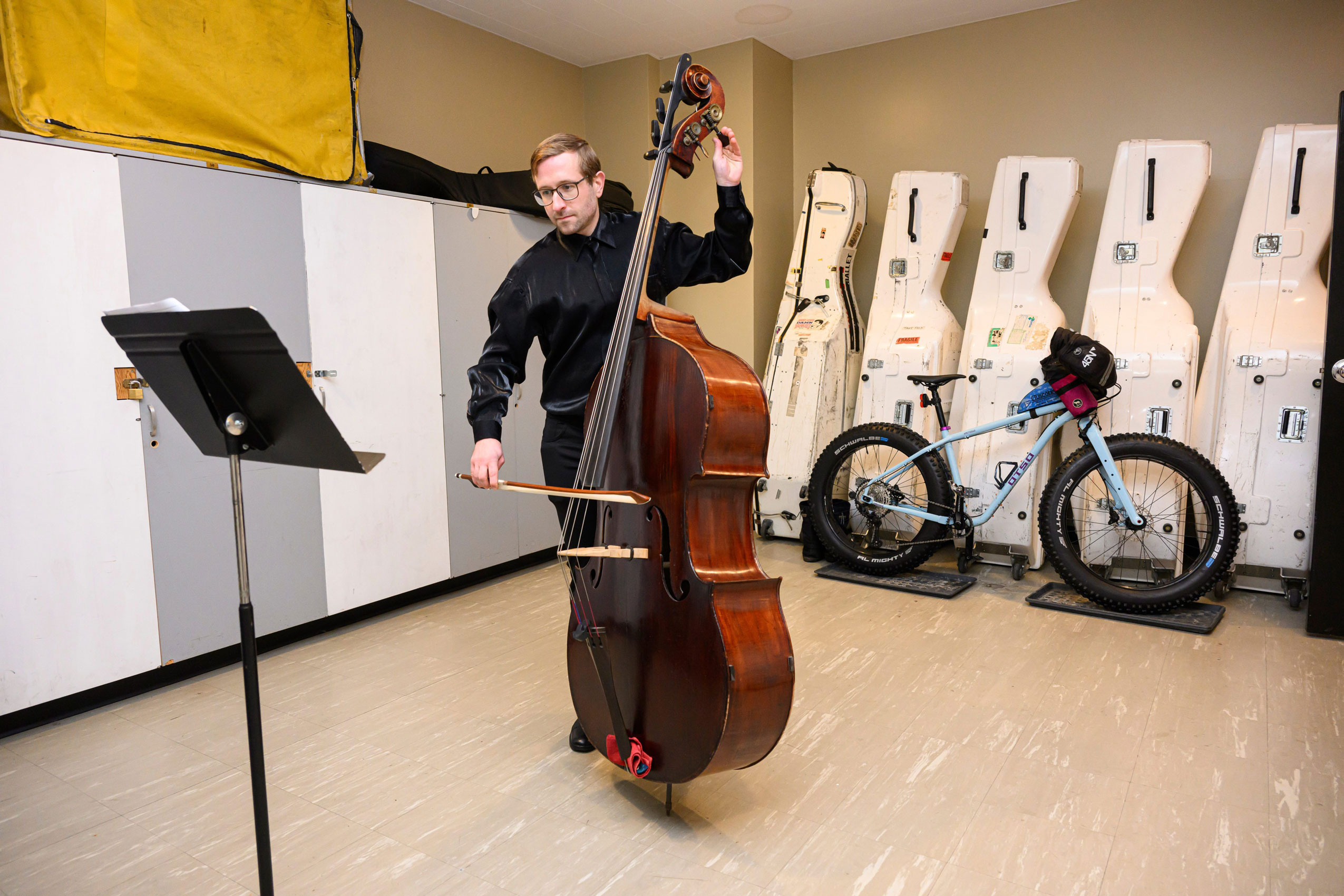 A Winnipeg Symphony Orchestra performer tunes up their instrument as a bicycle is parked in the background amid bass storage containers