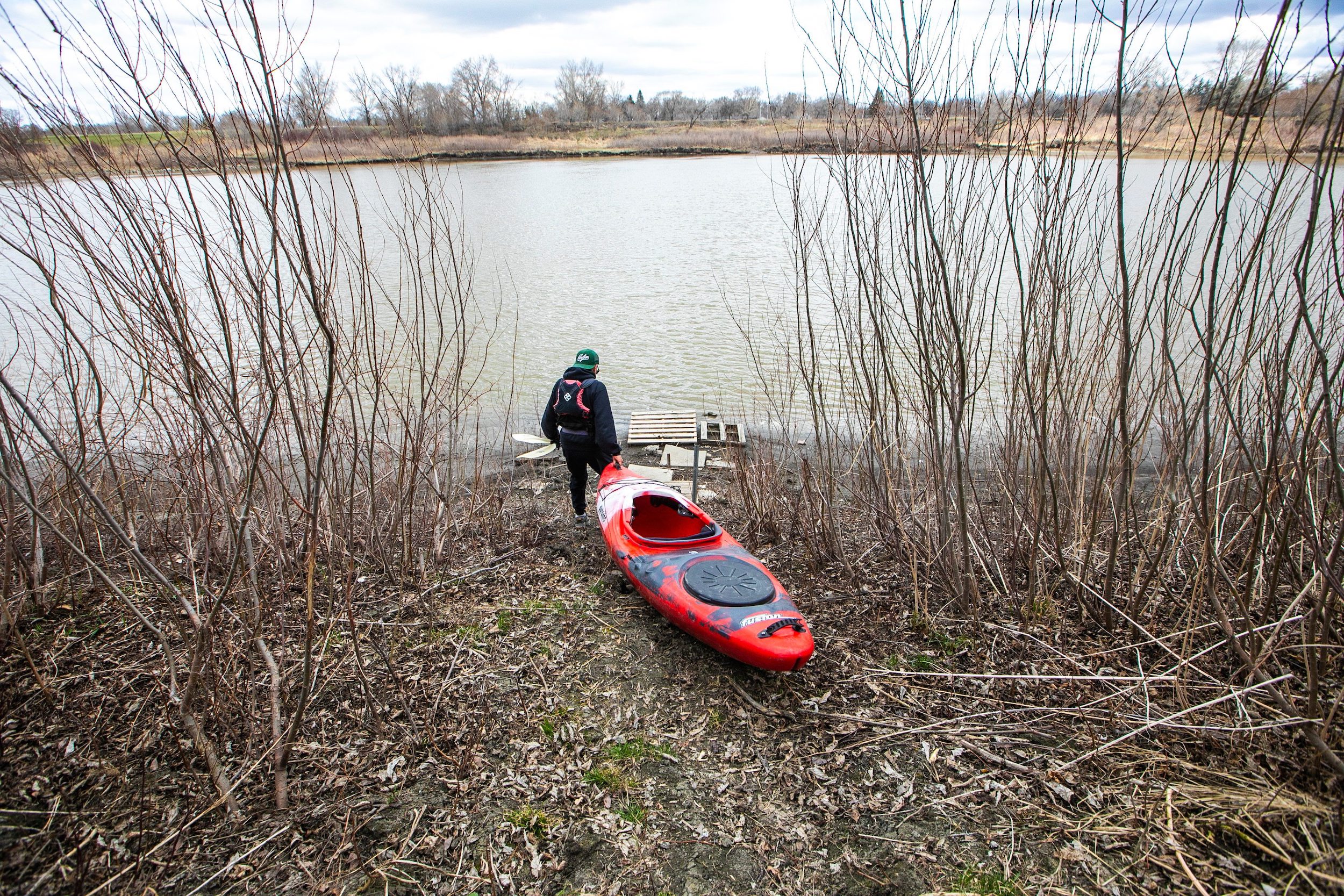A man brings his red kayak down to the Red River in early spring