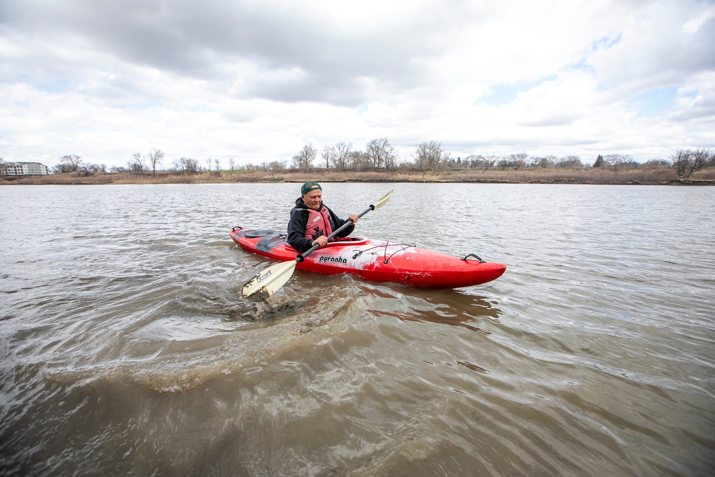 A man in a backwards ball cap kayaks on the murky-brown Red River in early spring